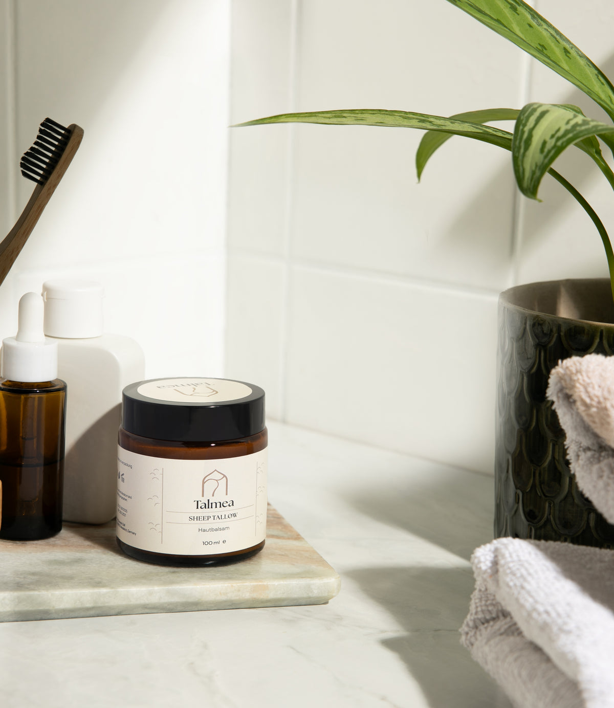 Talmea Sheep Tallow Hautbalsam im Badezimmer neben Zahnbürste, Ölflasche und Handtüchern