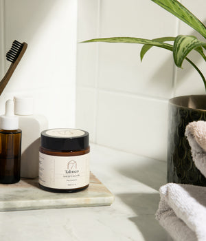Talmea Sheep Tallow Hautbalsam im Badezimmer neben Zahnbürste, Ölflasche und Handtüchern