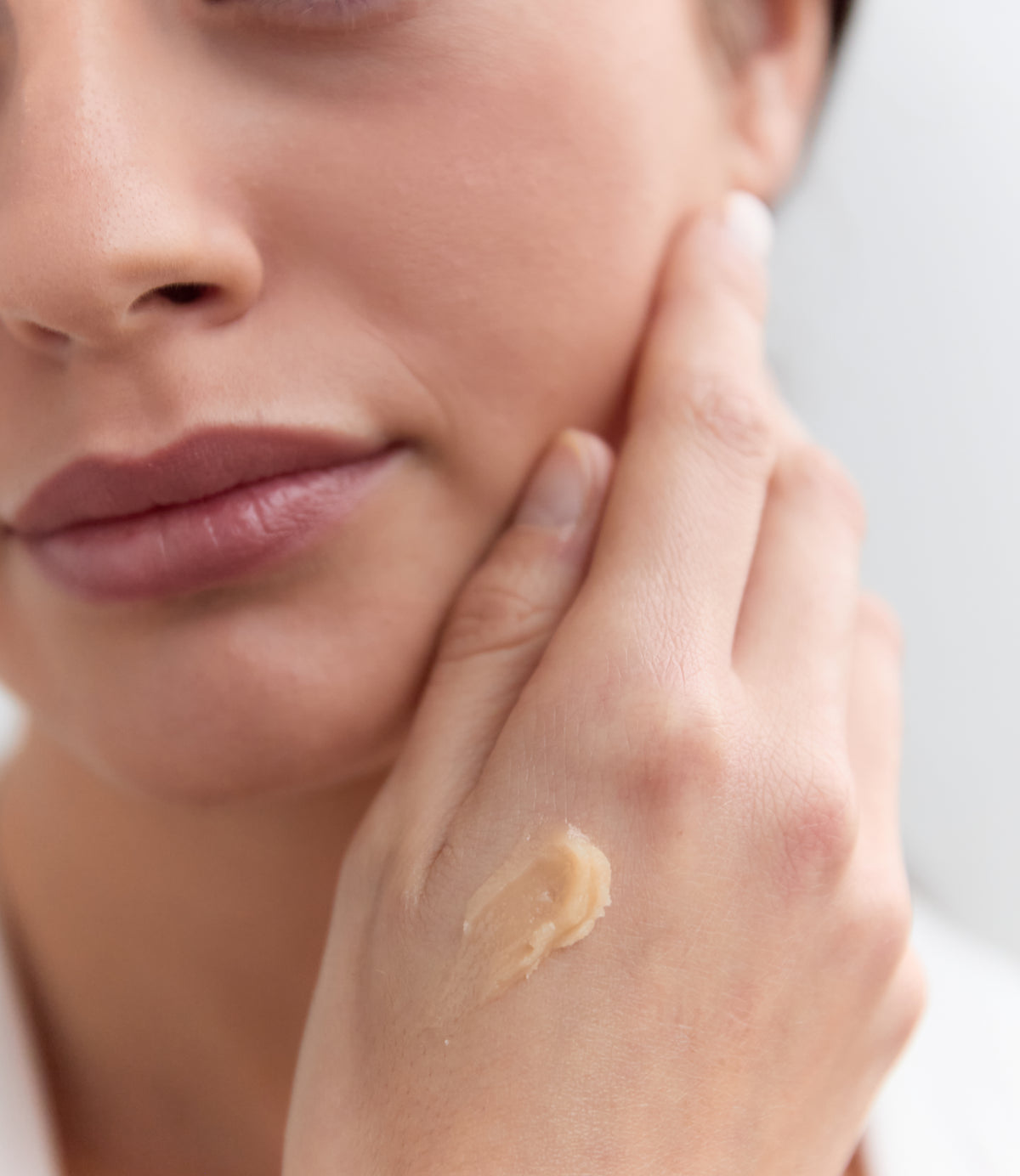 Frau berührt Gesicht mit Creme auf Handrücken