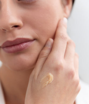 Frau berührt Gesicht mit Creme auf Handrücken